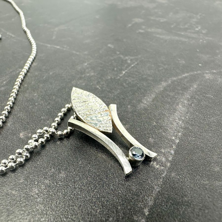 a marquise shape piece of silver cast in cuttle fish bones, with added sapphire blue CZ