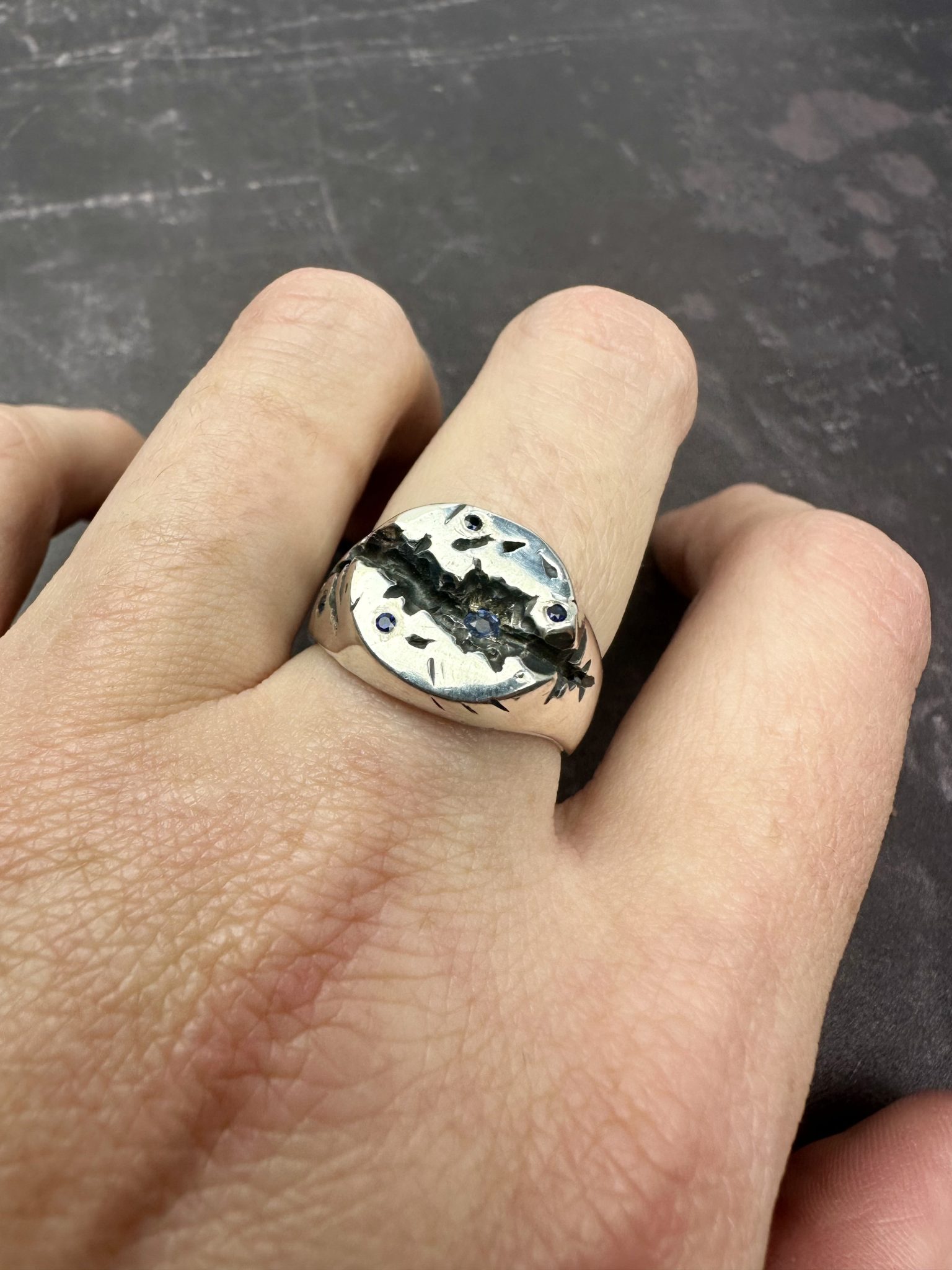 A sterling silver round signet ring, with a deep crevise handcared and scattered with sapphires.