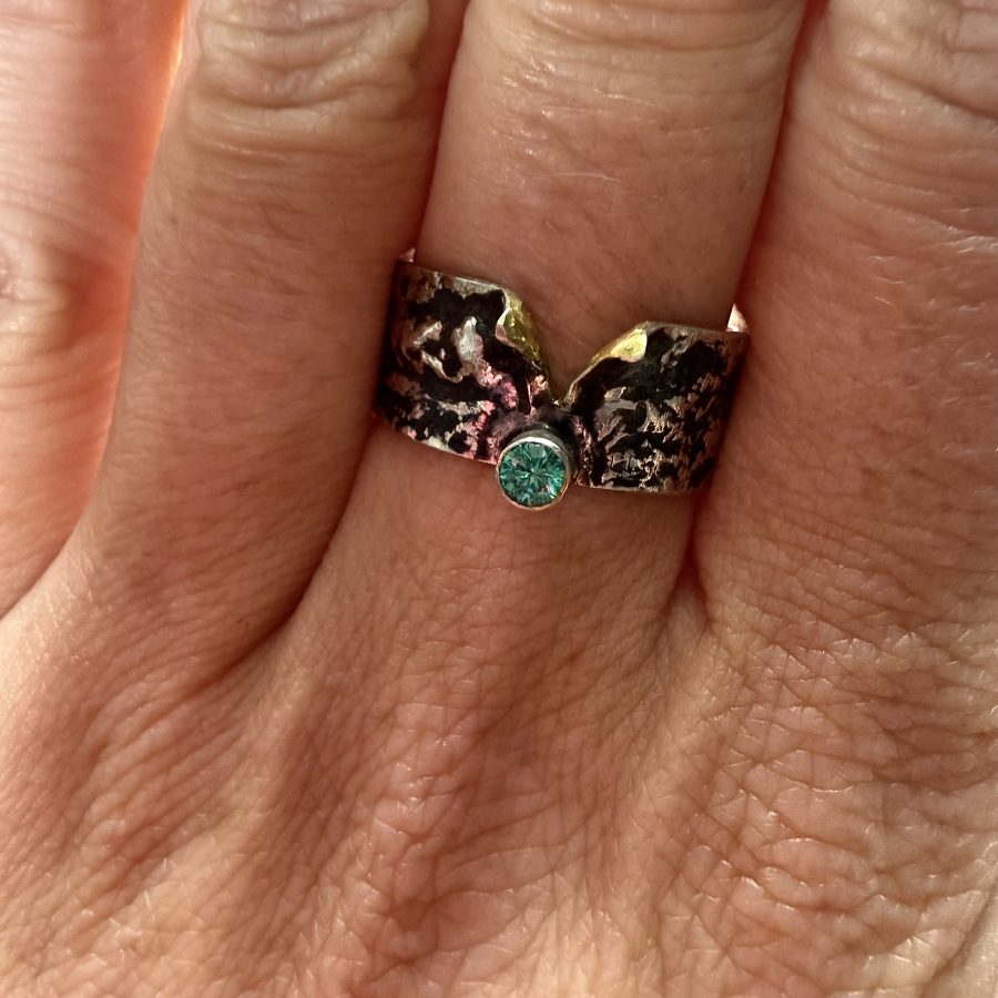 A sterling silver ring, reticulated with a tube set stone and a dot of gold peeking through the gap.